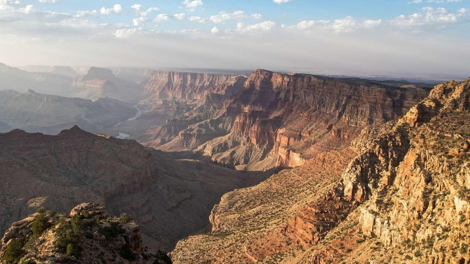 Colorful canyon walls and the Colorado River stretch into the distance beneath a blue sky.