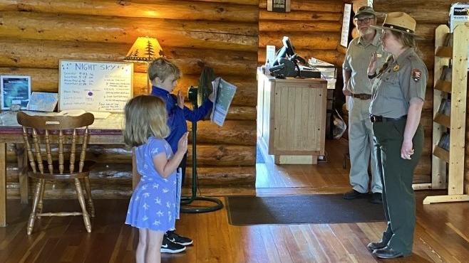 A ranger stands in front of two children and all have their right arms raised.