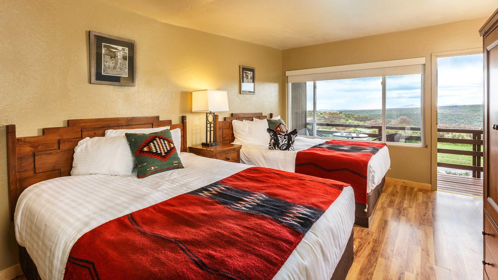 Two beds covered in geometric red blankets and pillows. View of hills outside windowed balcony.