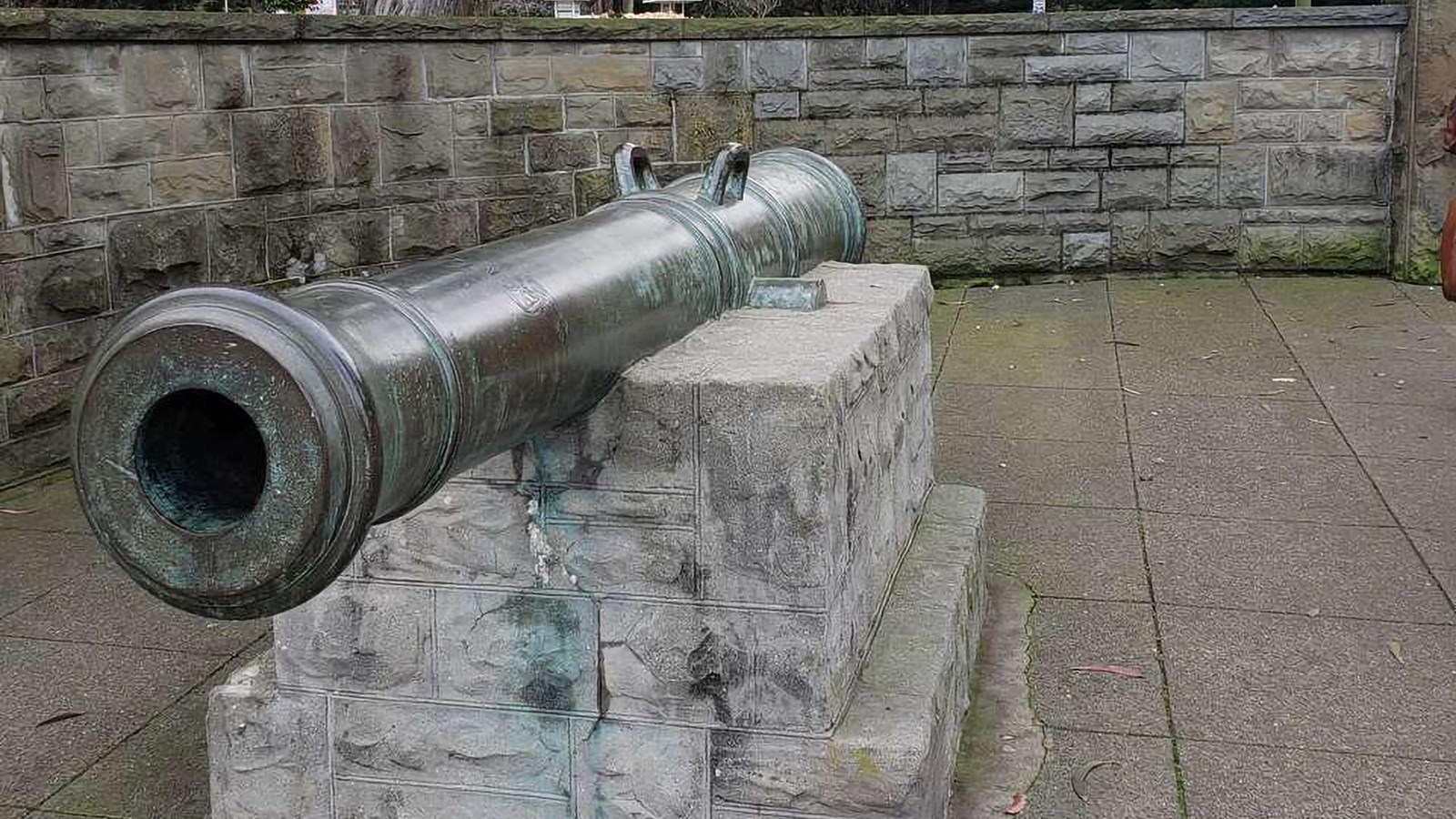 Bronze cannon outside Lombard gate, with stone wall and trees behind 