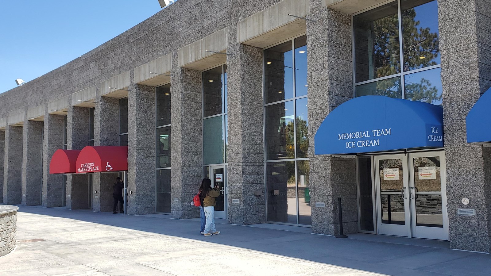 Gray building with floor to ceiling windows and four awnings over the entrance ways.