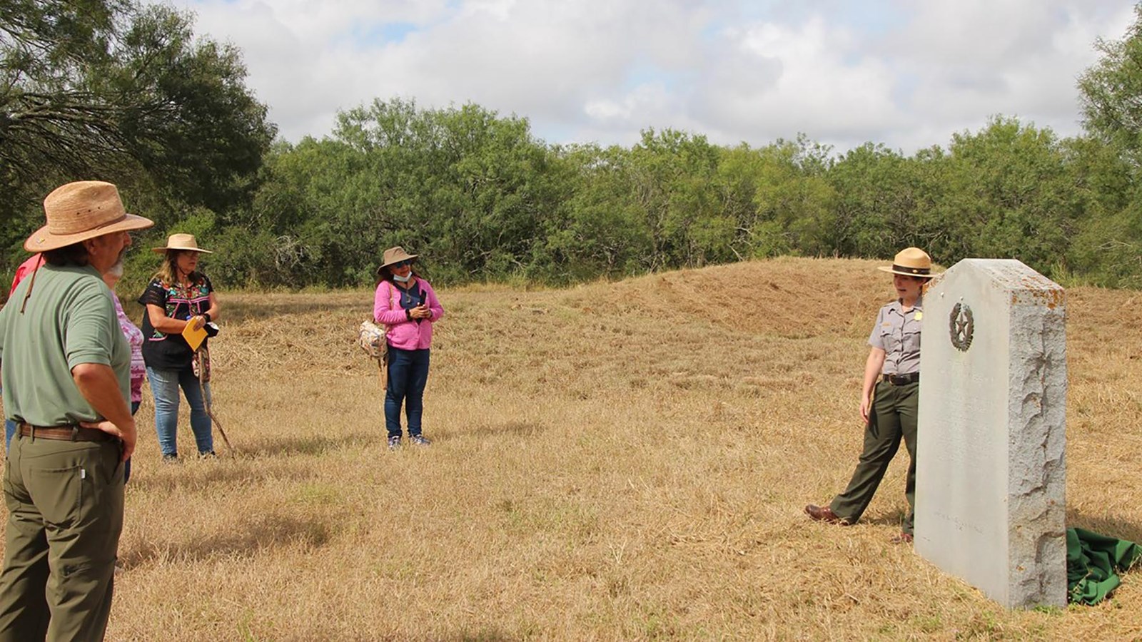 Visitors stand looking at a park ranger standing next to a historical marker.