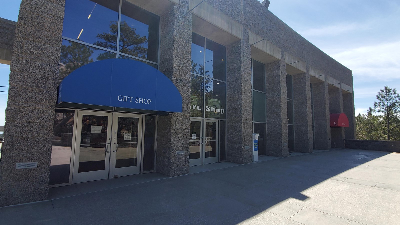 Gray building with floor to ceiling windows and a blue awning with the words 