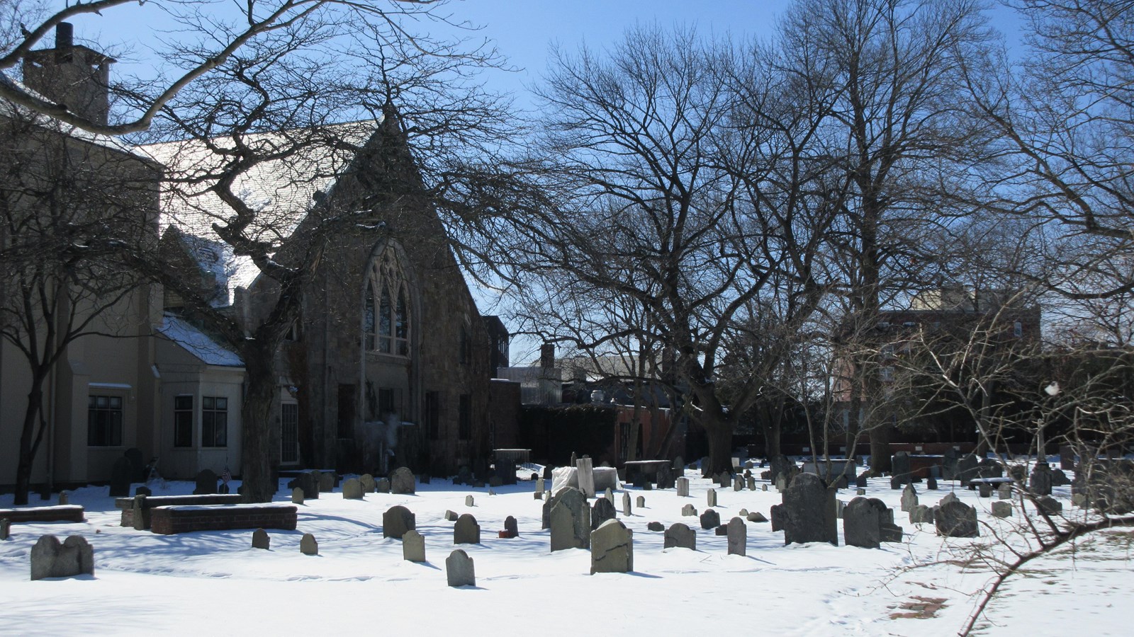 gravestones of various sizes and styles fill open space covered in snow, with church at left
