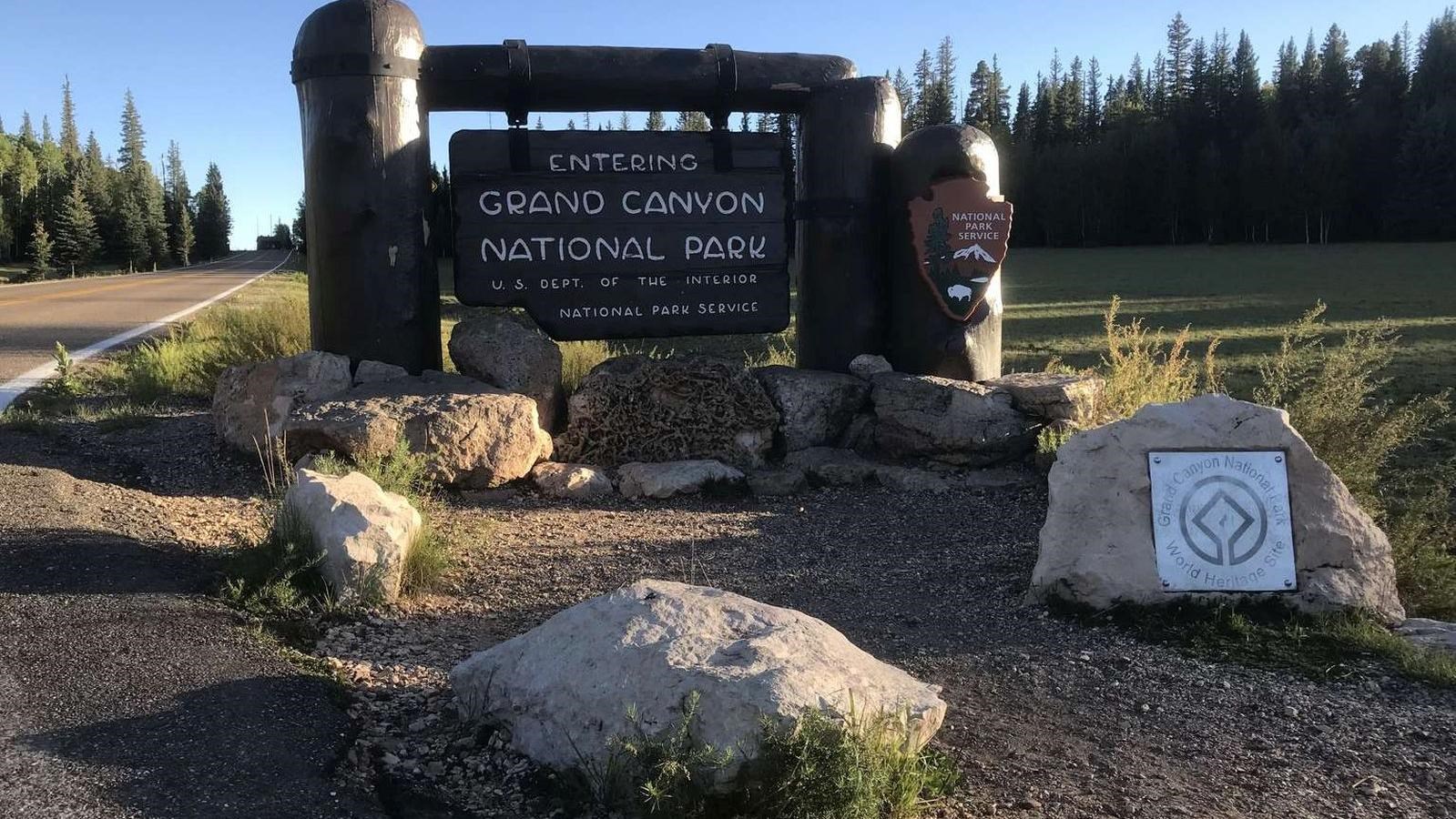 A large brown wooden sign suspended by large wooden pillars reads Grand Canyon National Park