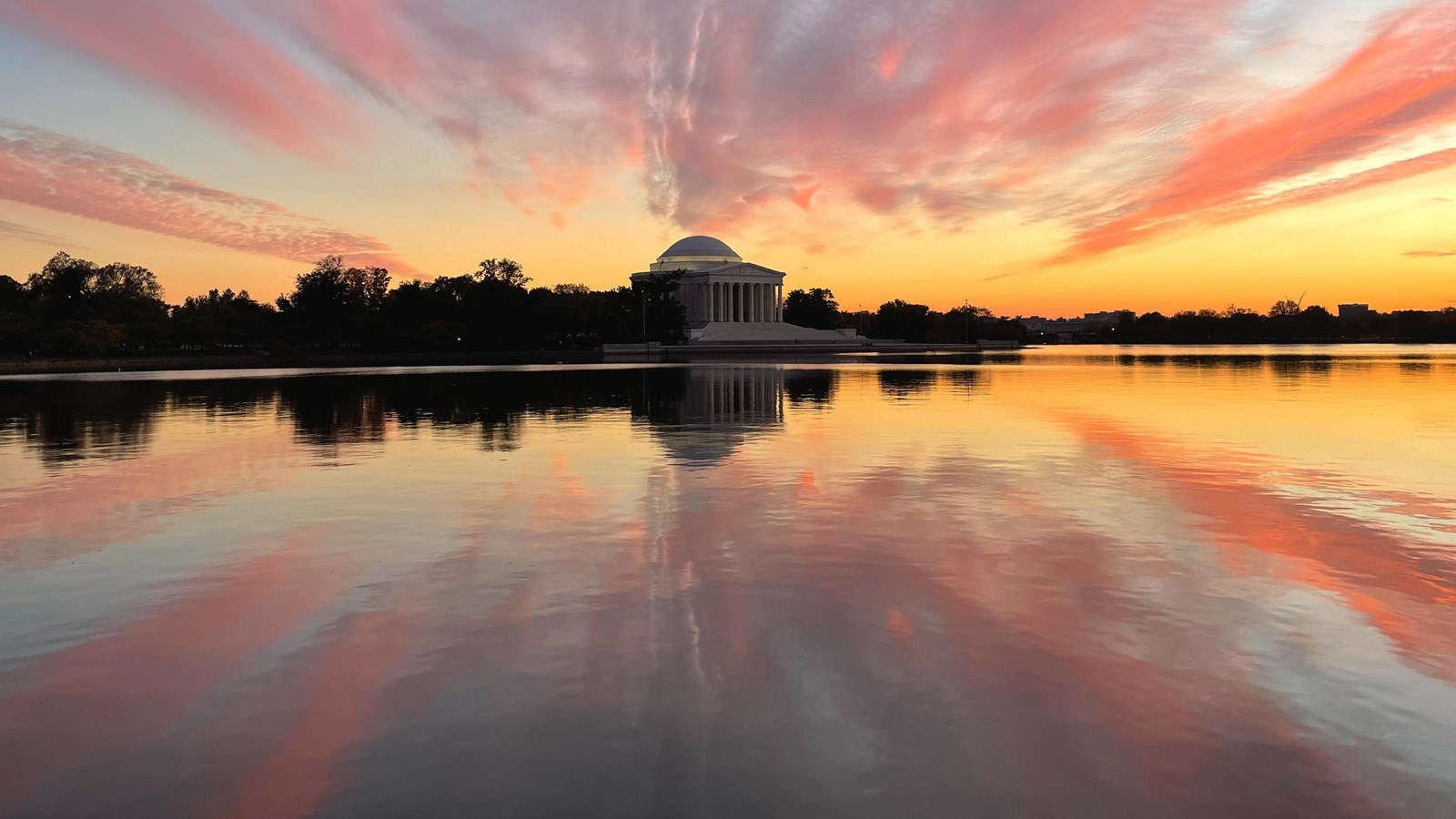 Body of water with colonnaded memorial in the background and a colorful sunset