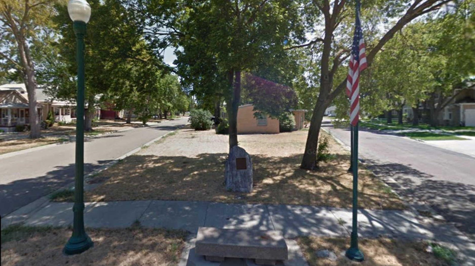 small city park between two residential streets.  A large boulder has a bronze plaque with a memoria