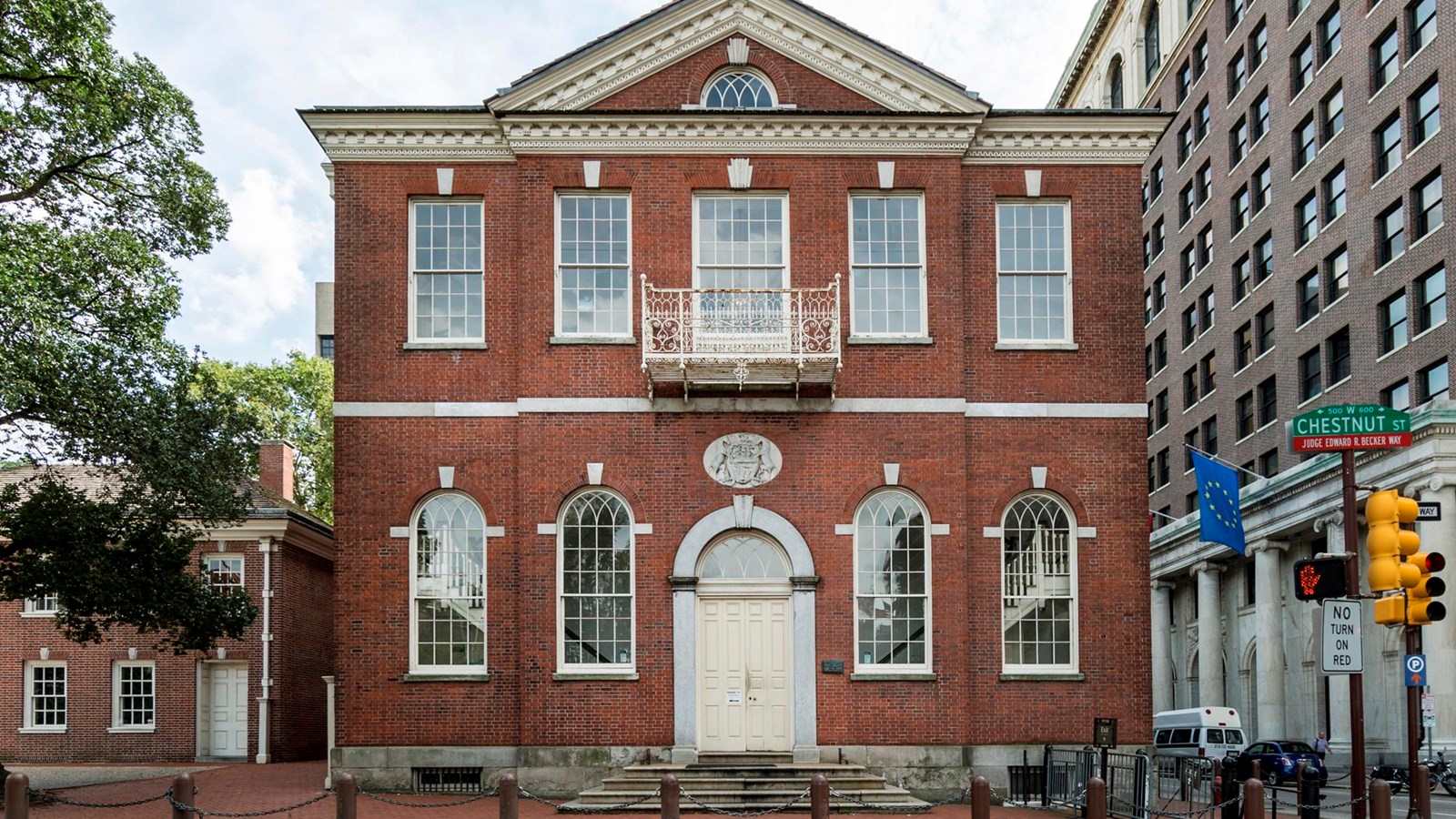 A color photo of a tall, two story red brick building with a triangular pediment.