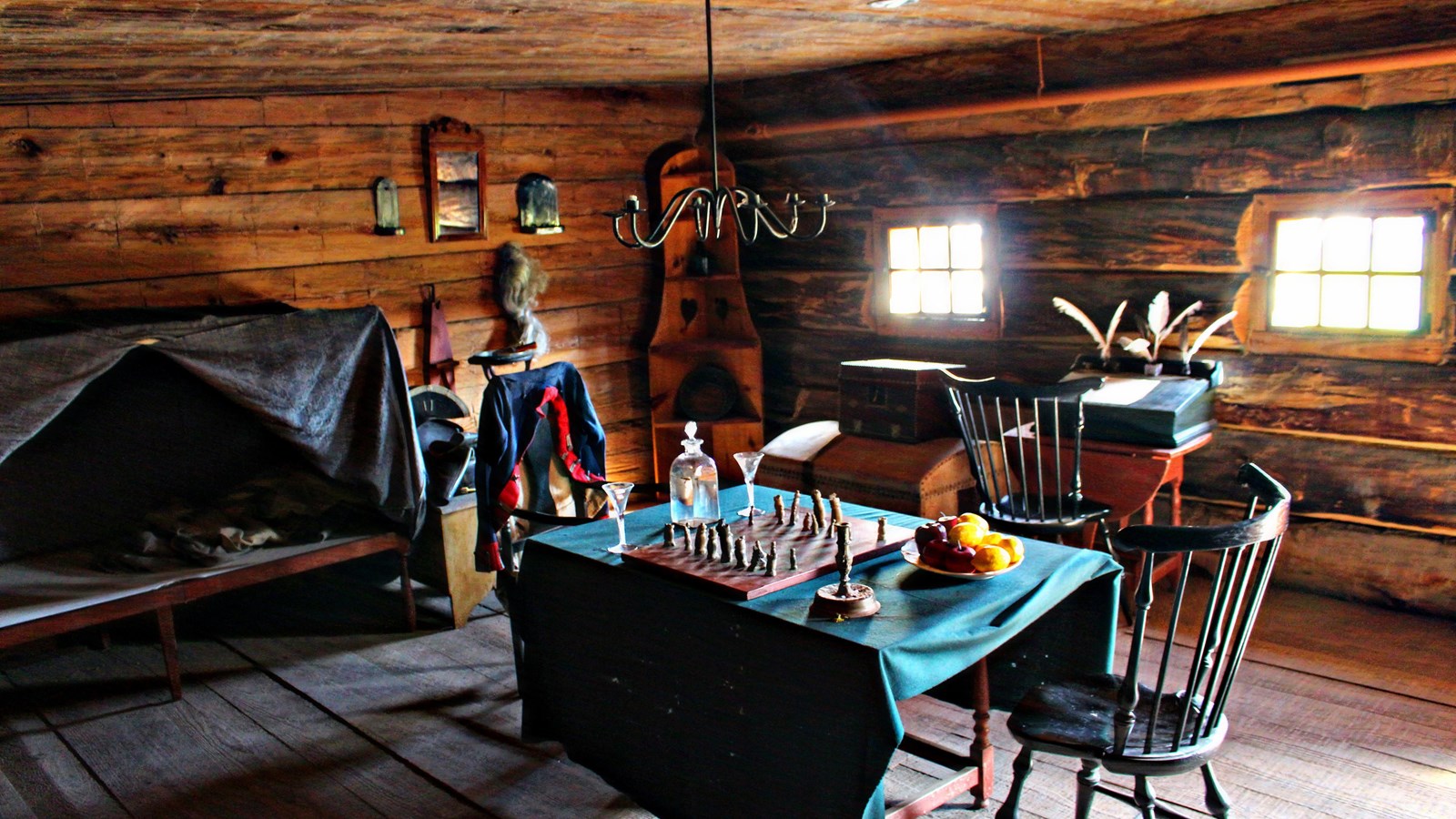 A room with a small canopy bed and a table with a chess game and fruit on it. Two chairs sit at it.