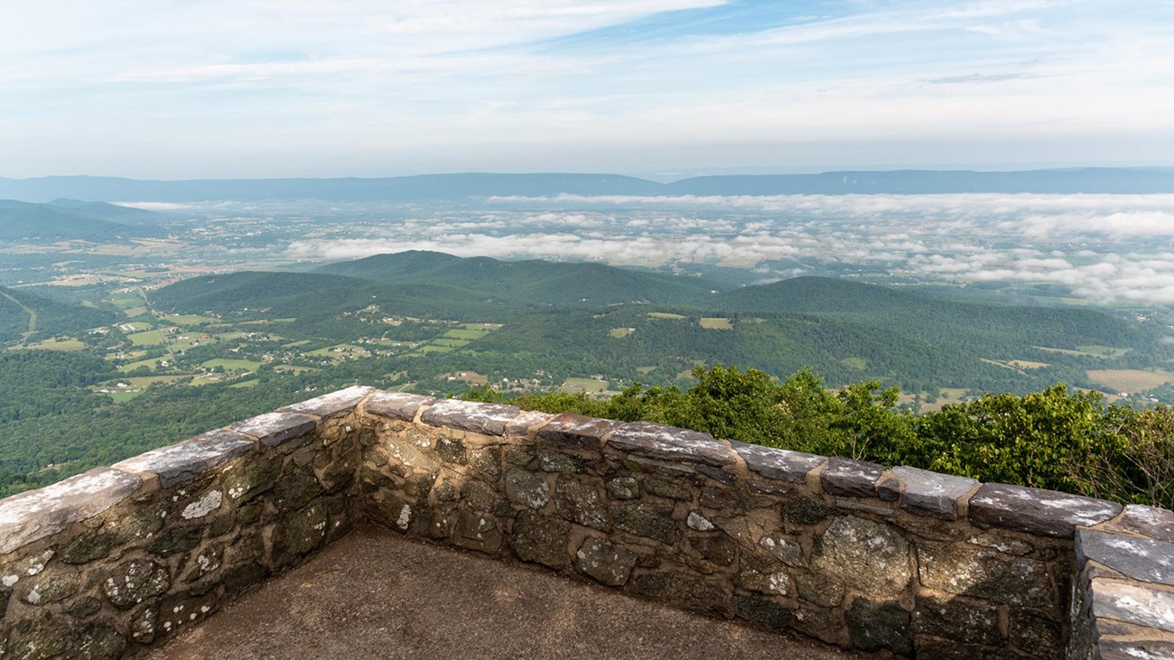 A stone platform with a view of a valley below and blue mountains beyond.