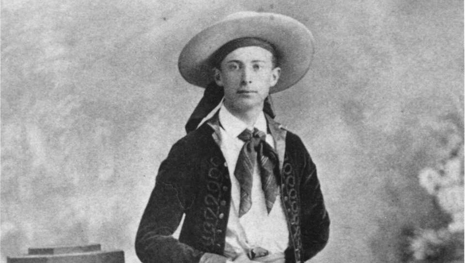 Historic photo of man posing for picture with black cowboy pants and jacket and white hat.