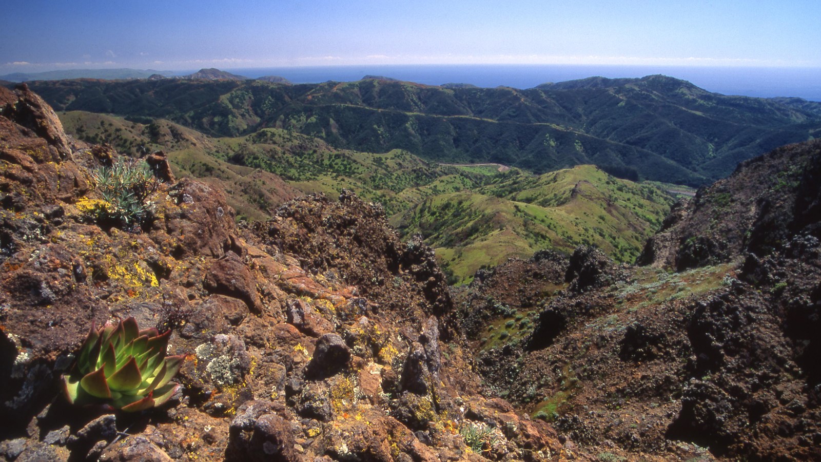 View of low mountain range with ocean in background from a high peak. 