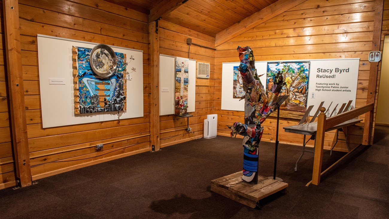 An interior view of a room with a large sculpture on the floor and colored art on the walls.