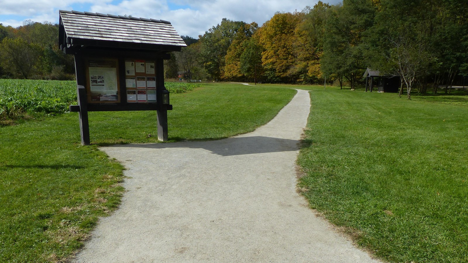 Firm, flat, unpaved trail curves from kiosk, past restrooms, to the distant red bridge in the trees.