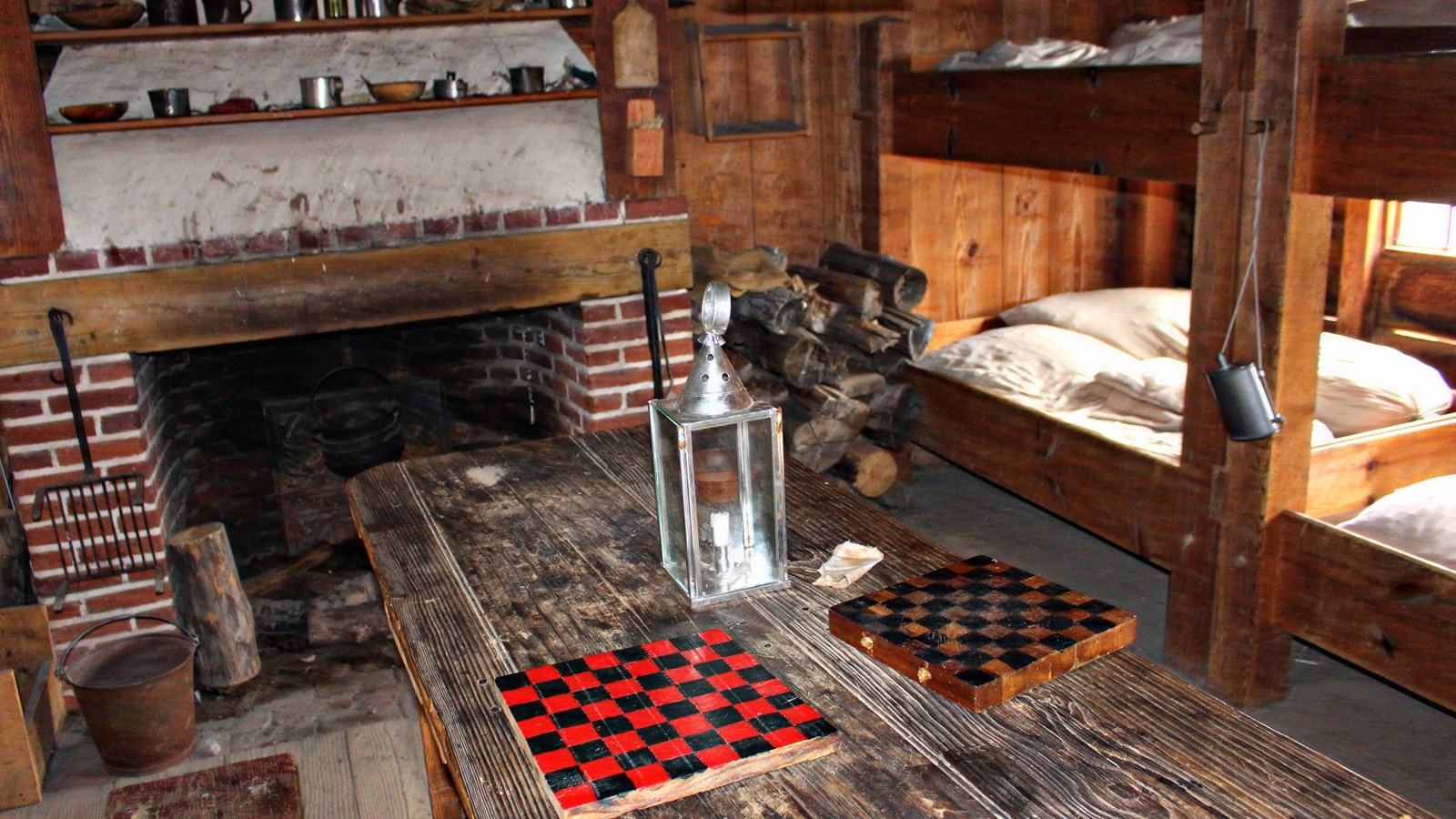 A room with multiple large wooden bunk beds, a large fireplace, and a table with checkers sitting it