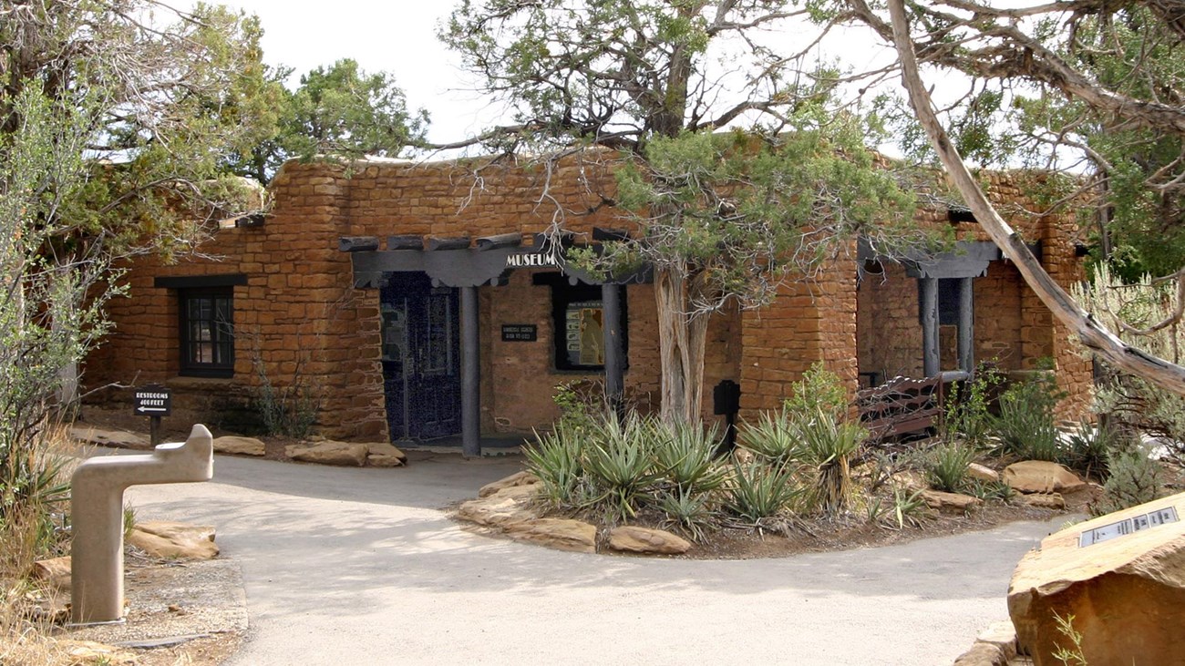 Rock and timber building surrounded by yucca, brush, and trees.