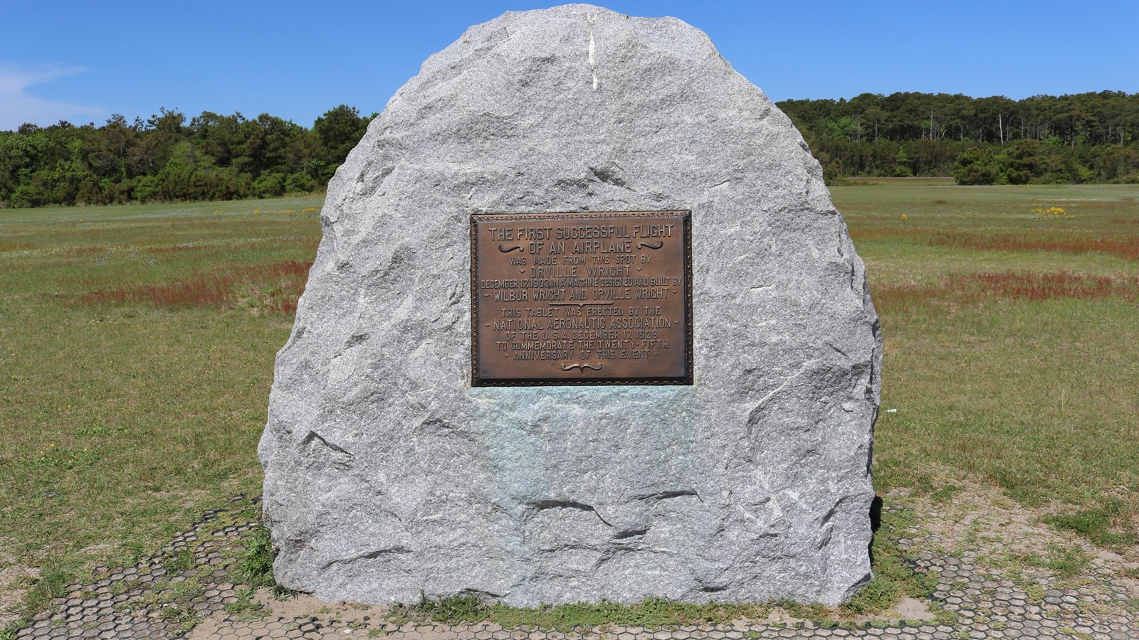 A large, granite boulder has a bronze plaque centered in it. 