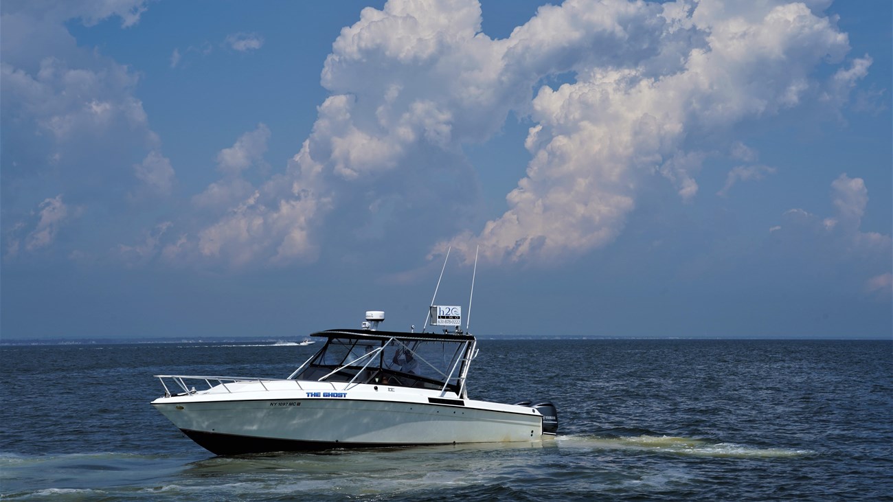 A mid sized boat floats before a dramatic cloud-filled sky. 