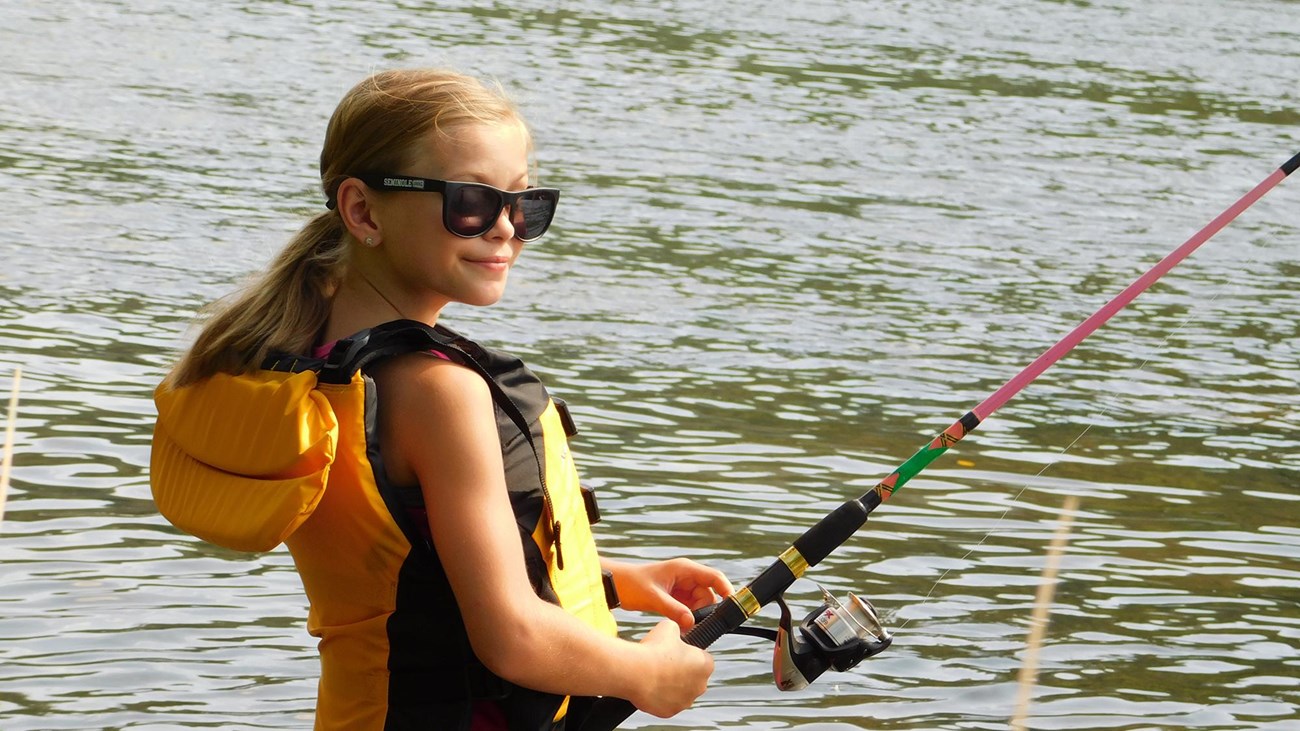 girl wearing life jacket and fishing in a river
