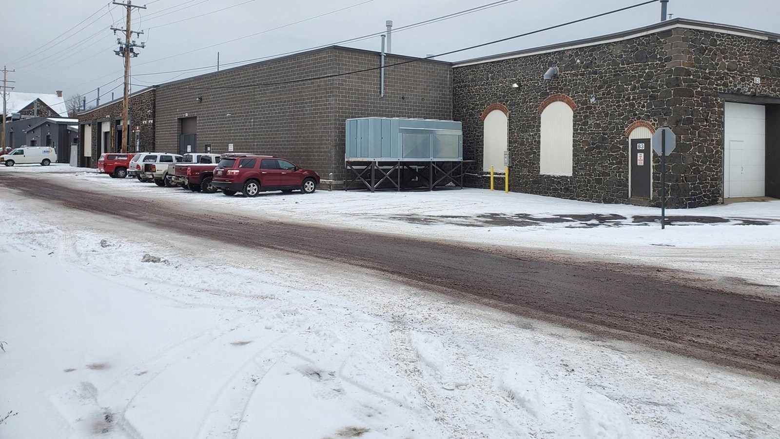Winter scene of dark-grey single story poor-rock building with dark-grey brick addition.