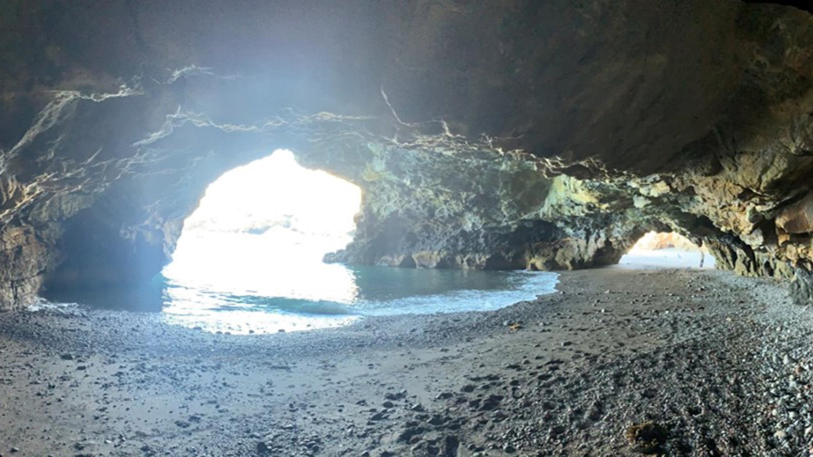 looking from inside a sea cave out towards ocean. cave has 3 openings.