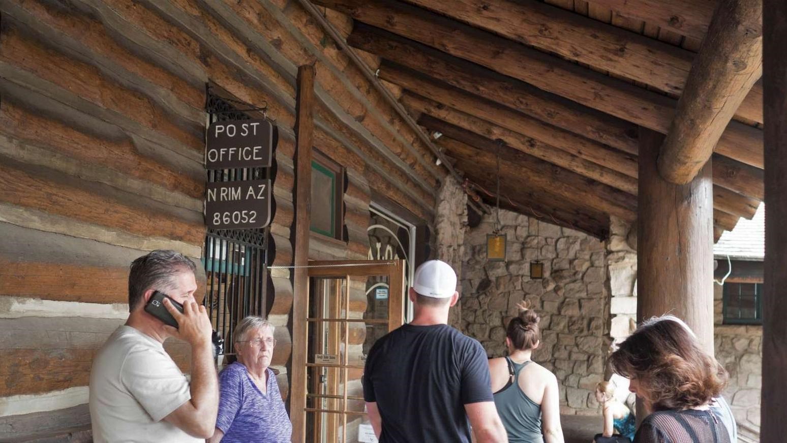 A crowd of people gather in front of the old white and brown wooden Post office sign
