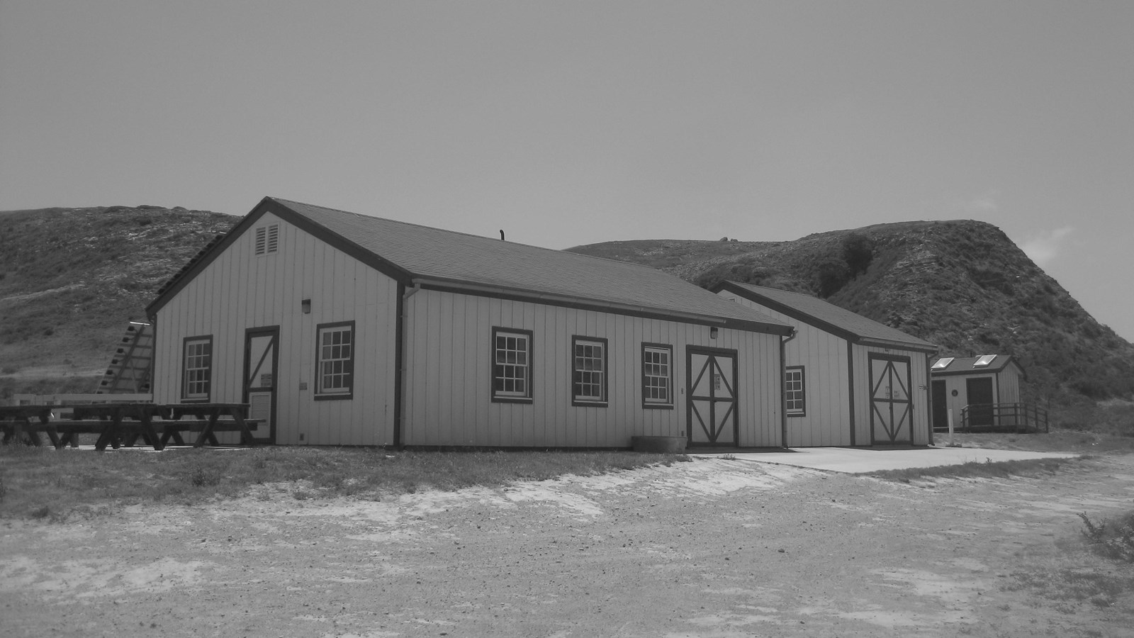 Two wood buildings side by side with windows doors and picnic tables out front.