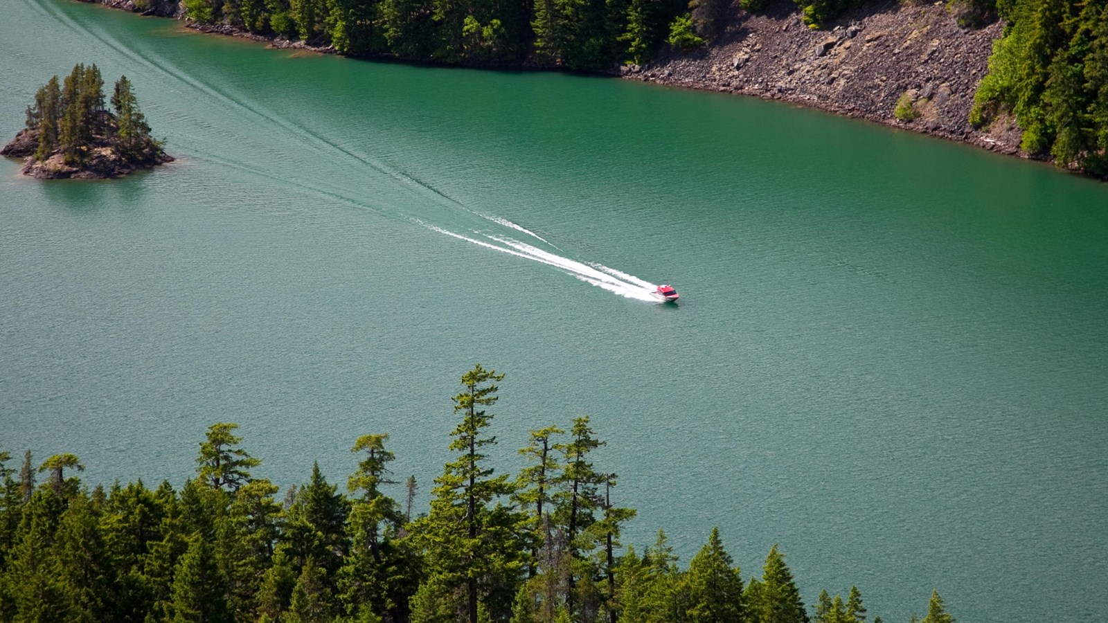 A motorboat on a green lake surrounded by mountains.