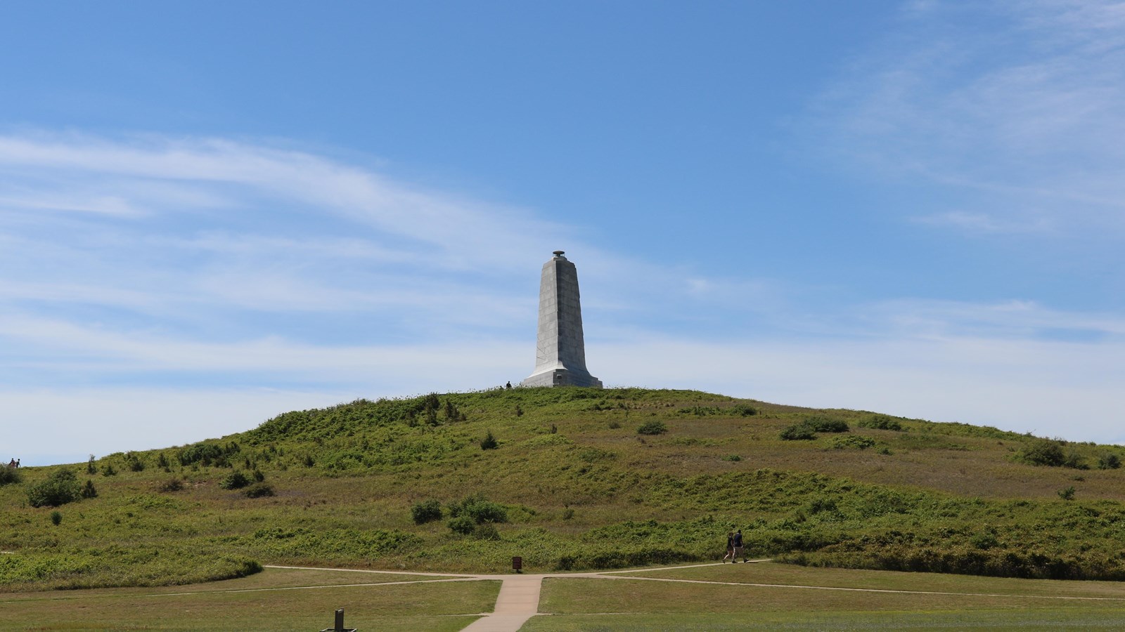 The Wright Brothers Monument sits on top of a tall hill, covered in grass and vegetation.