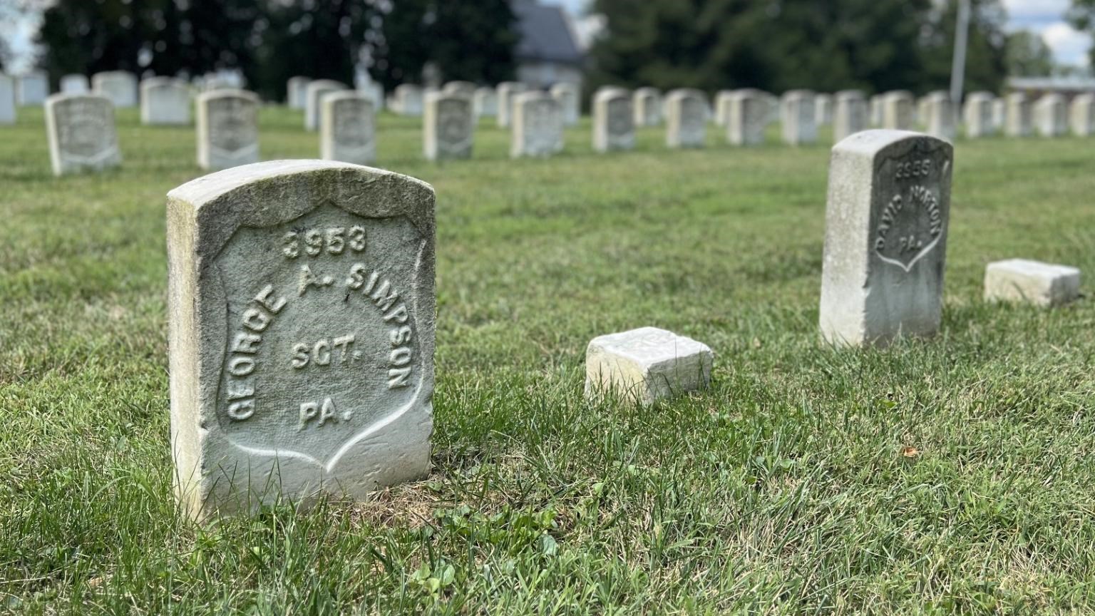 white grave stone surrounded by other grave stones with white cloud blue sky background
