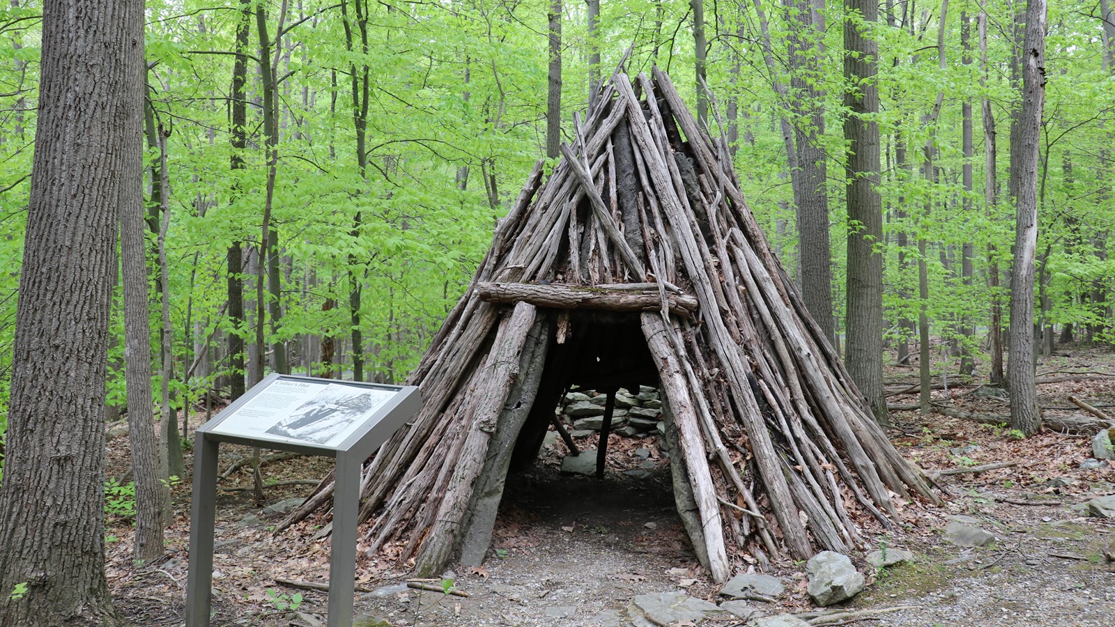 A triangular shelter made of stacked logs and sticks.
