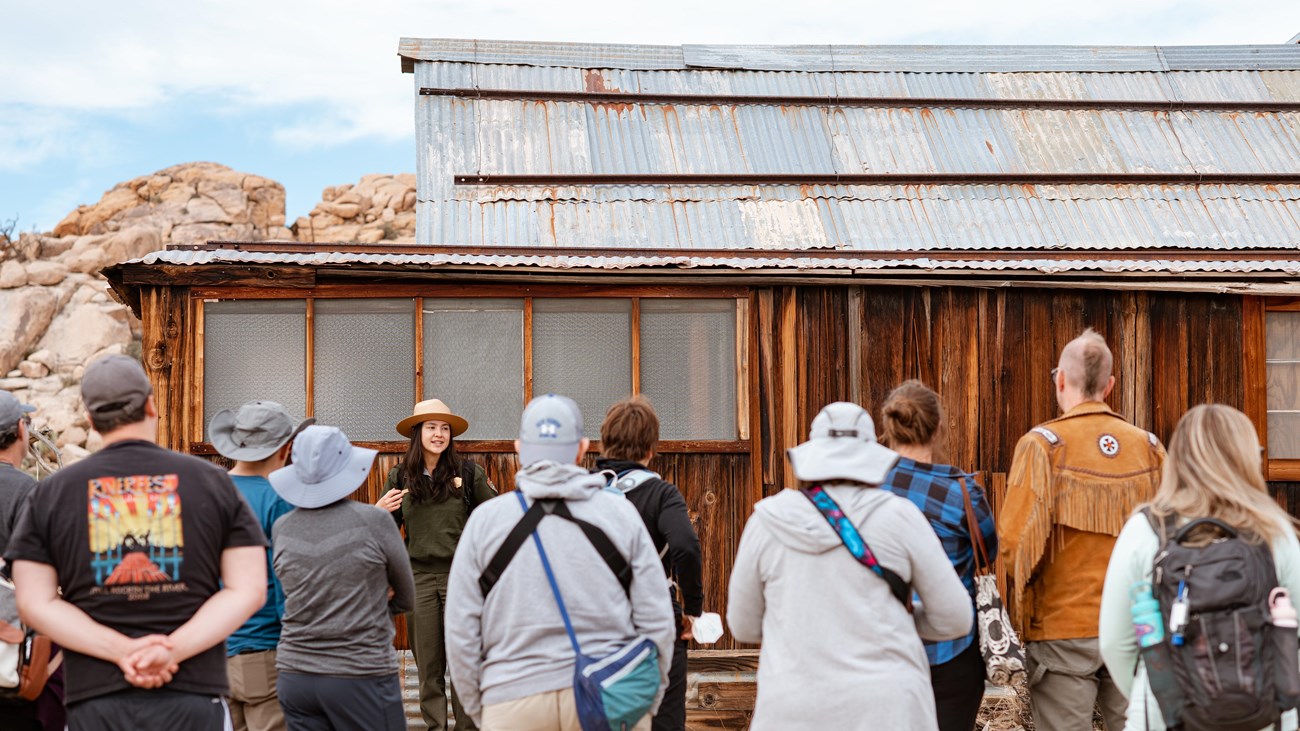 A park ranger talks to a group of visitors in front of a rustic building