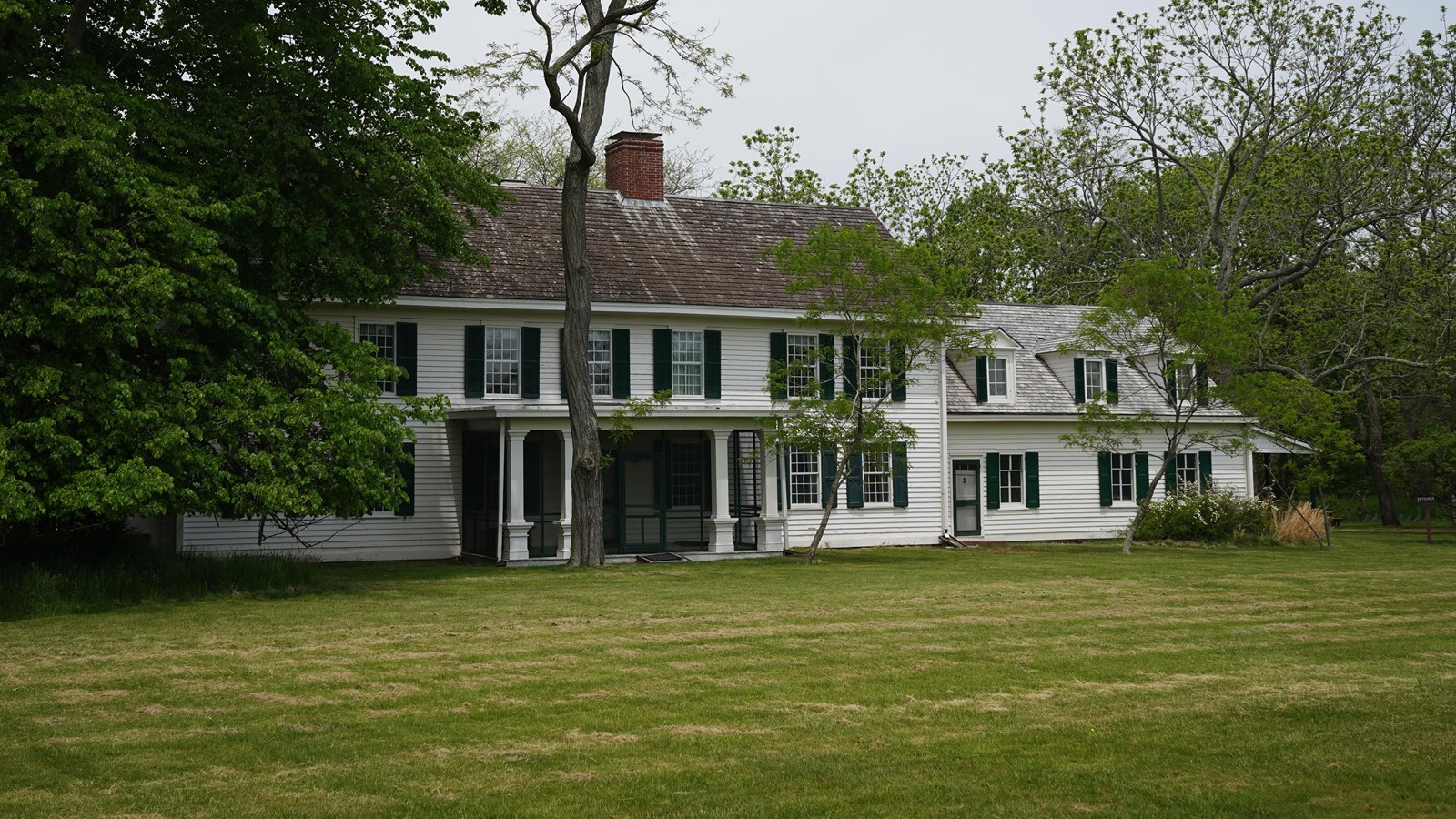 A white manor house with white trim is surrounded by trees.