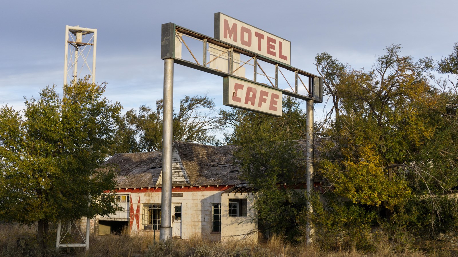 A white and red building surrounded by trees. A large white sign with red text reads