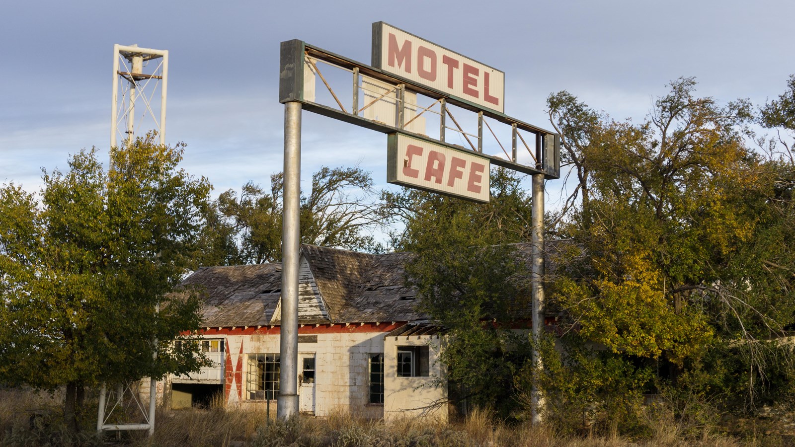 A white and red building surrounded by trees. A large white sign with red text reads 