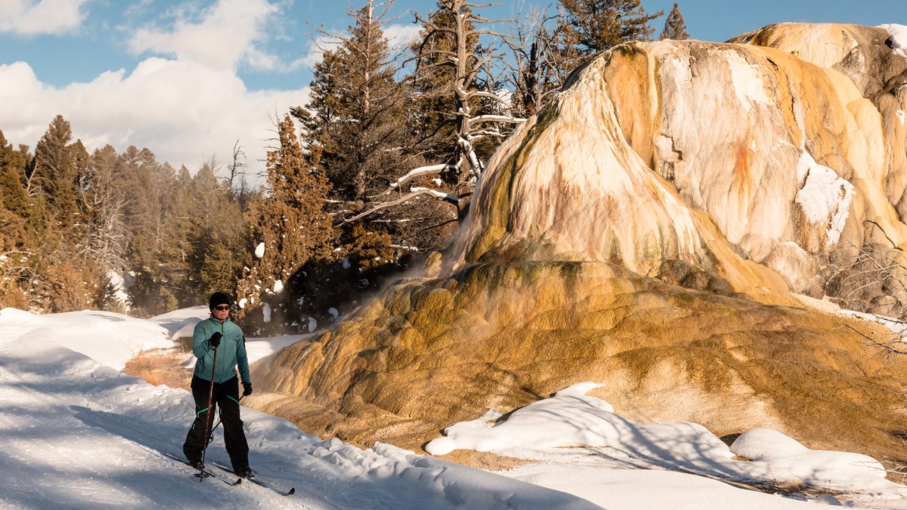 A cross-country skier passes a thermal feature as they ski along a trail.