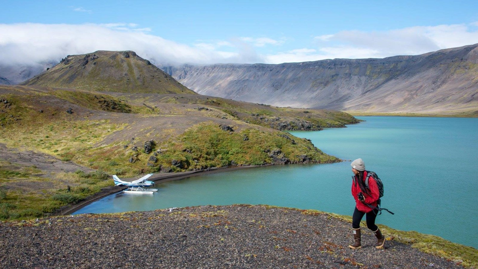 A hiker on a hill above a lake with a float plane