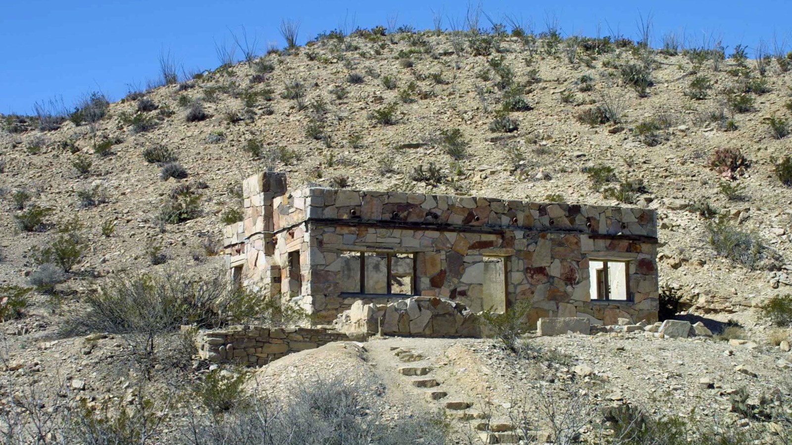 A rock house with lots of windows sits on a limestone hill