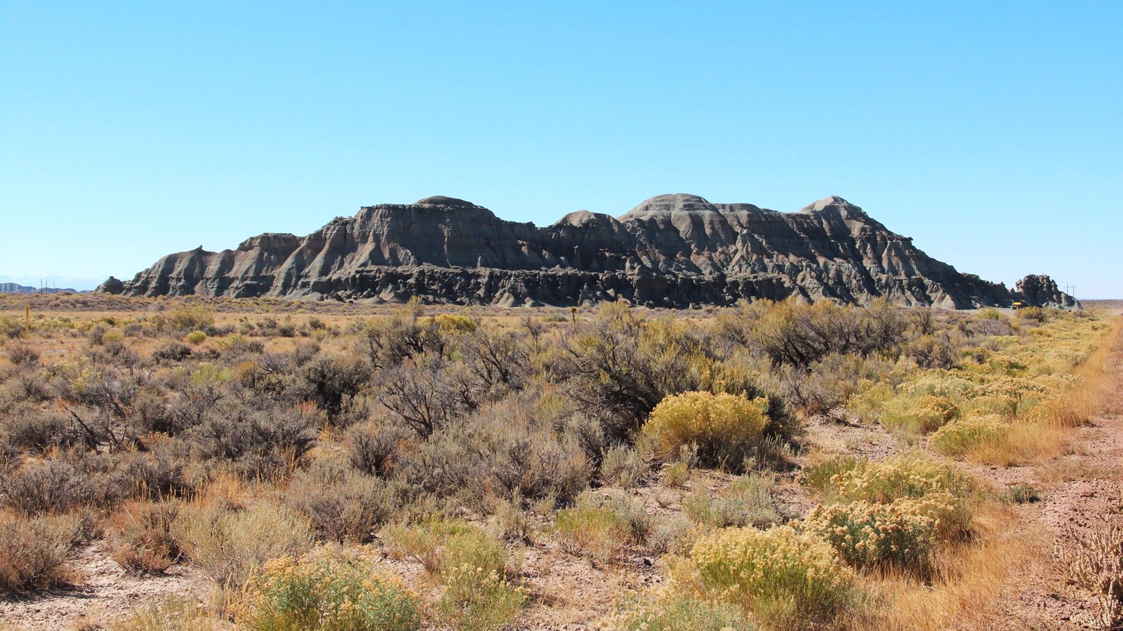 Church Butte rises above sagebrush, with colorful bands and rounded peaks under blue sky.