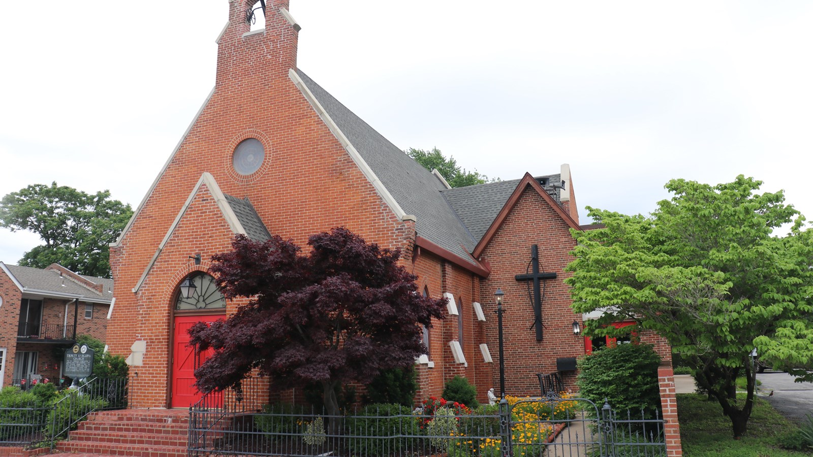 A small brick church with a bell tower with an enclosed flower garden on the side.