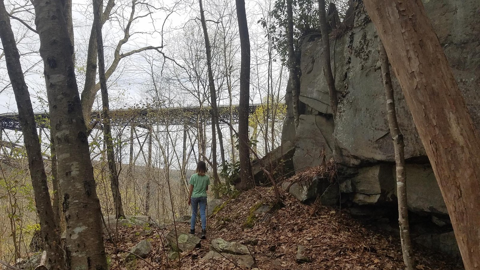 A hiker on rocky trail about to pass under a large bridge