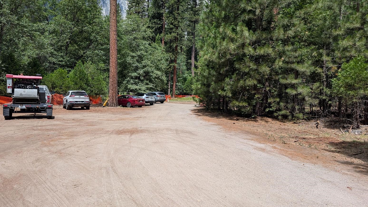 Dirt parking lot with cars in it surrounded by trees