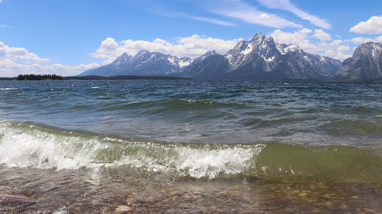 Waves crash on the shore of a lake at the base of a mountain range.
