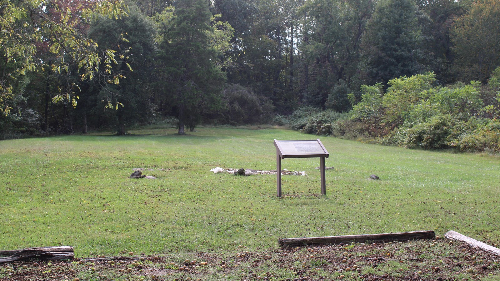 A green field with building foundation stones in the center and a sign in front.