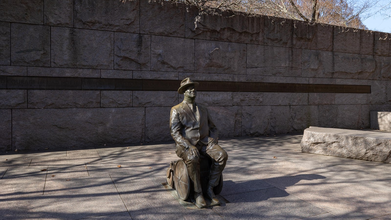 A statue of a man wearing a hat and suit sitting in a wheelchair.