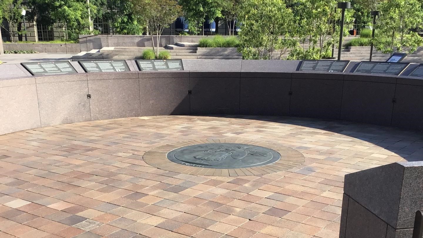 Open plaza surrounded by waist high circular wall. There is a metal medallion in the center.