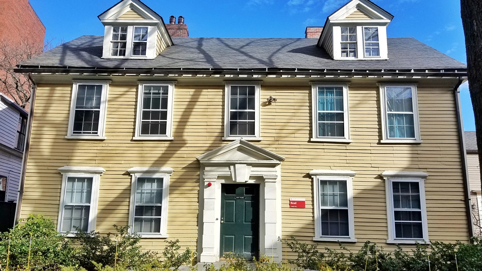 two-story yellow house with symmetrical facade, two dormers and chimneys, and a central green door