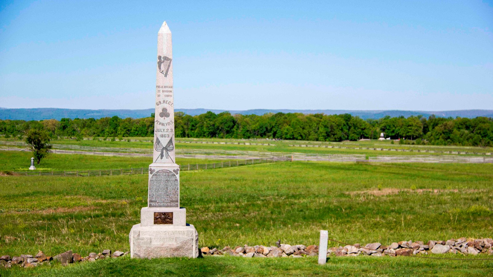 A obelisk shaped monument next to a field and stone wall