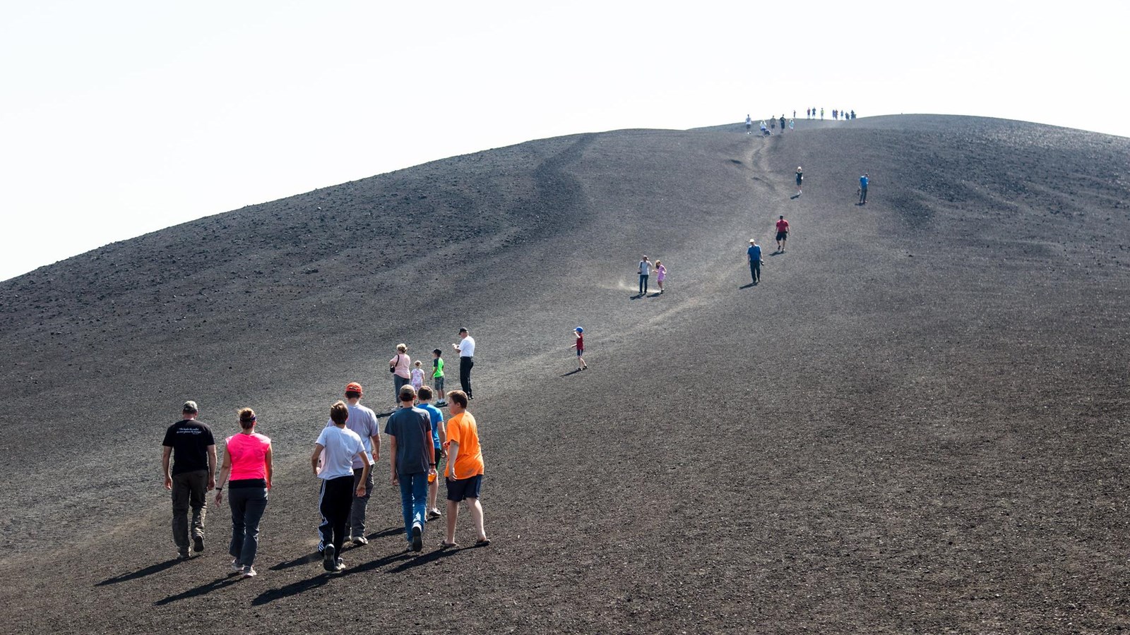 Hikers head up a steep trail on the barren side of a cinder cone.