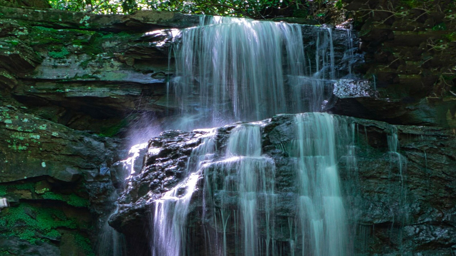 Water flowing gently over stepped sandstone rocks sticking out from a rocky face
